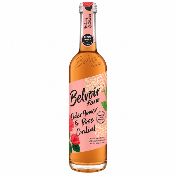 A bottle of Belvoir Farm Elderflower & Rose Cordial syrup, filled with a golden-amber liquid, featuring a pink label with illustrations of red roses and a gold glitter pattern, on a solid white background.