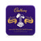 A square purple Cadbury Dairy Milk tin with gold lettering and an illustration of a milk carton, sitting on a scale in a store setting.