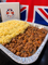 A foil pan of traditional British beef and peas with mashed potatoes, with a white box labeled 'AFFERS OF KENWICK' and a Union Jack flag in the background.