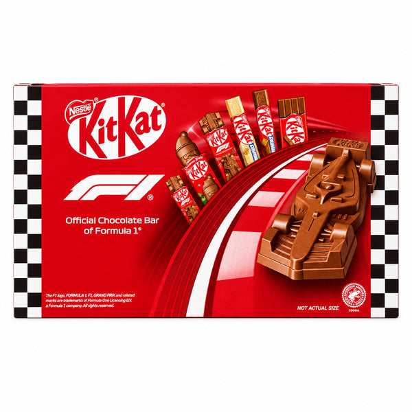 A box of Nestle KitKat chocolate bars featuring Formula 1 branding, displayed on a stone surface with a blurred wooden background.