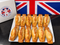 A white rectangular plate holding ten golden-brown baked pastries arranged in two rows, with a white box and a Union Jack flag in the background. The box shows the brand name 'Nyers of Keswick'.