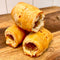 Three baked pastry rolls stacked on a wooden surface with a white tiled wall in the background.