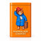 An orange rectangular tin of Paddington Bear Marmalade Cookies sits on a marble countertop with a blurred wooden background. The tin features an illustration of Paddington in his signature blue duffle coat and red hat, with the text 'MARMALADE COOKIES' printed at the bottom.