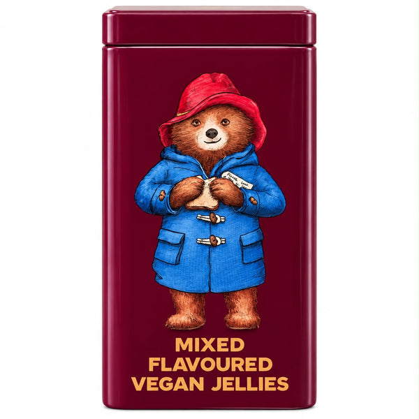 A rectangular dark red metal tin featuring an illustration of Paddington Bear in a blue duffle coat and red hat, with the text 'MIXED FLAVOURED VEGAN JELLIES' in yellow at the bottom.