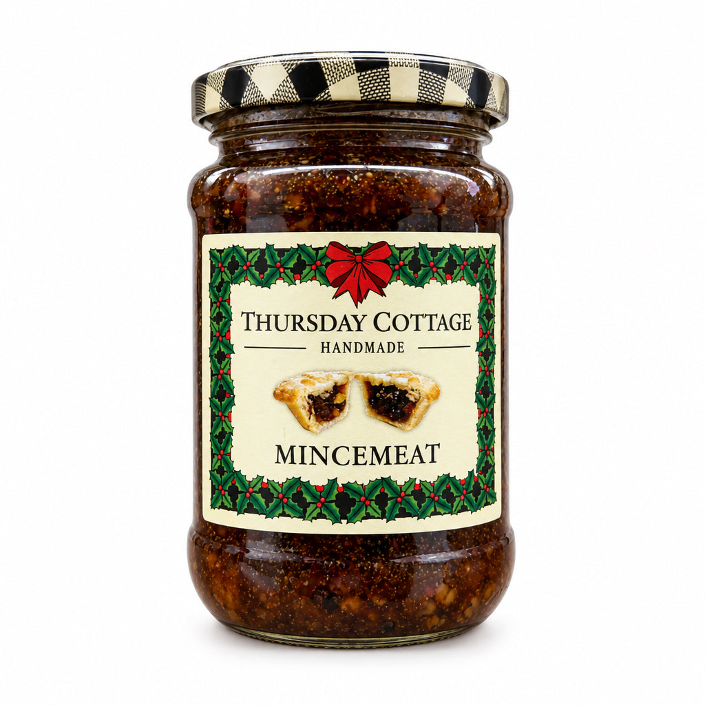 A glass jar of Thursday Cottage Handmade Mincemeat on a white background. The jar contains dark brown mince meat and has a cream-colored label with a red bow and green holly border, topped with a black and white checkered lid.