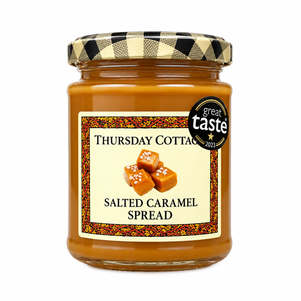 A jar of Thursday Cotton Salted Caramel Spread sits on a speckled stone countertop in front of a rustic wooden door. The jar has a black and beige gingham lid and a cream-colored label with a black circular 'Best Taste' badge.