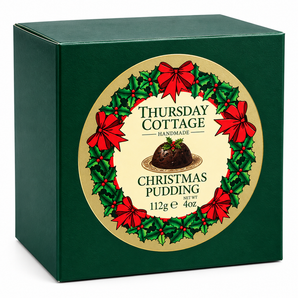 A dark green square box of Thursday Cottage Handmade Christmas Pudding, featuring a large circular gold label decorated with a green holly wreath and red bows.